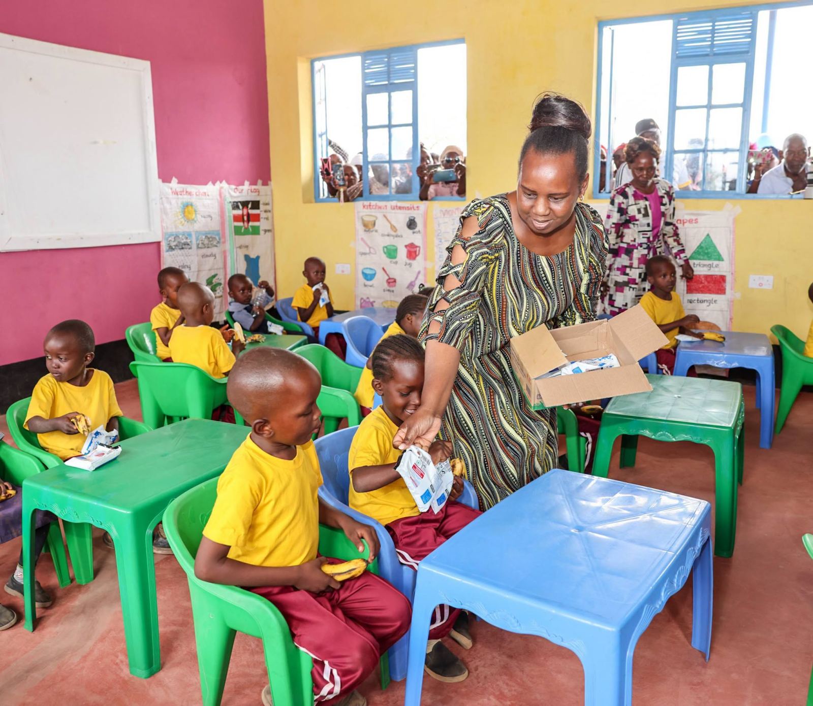 A teacher hands out milk to pupils in a brightly painted ECDE classroom