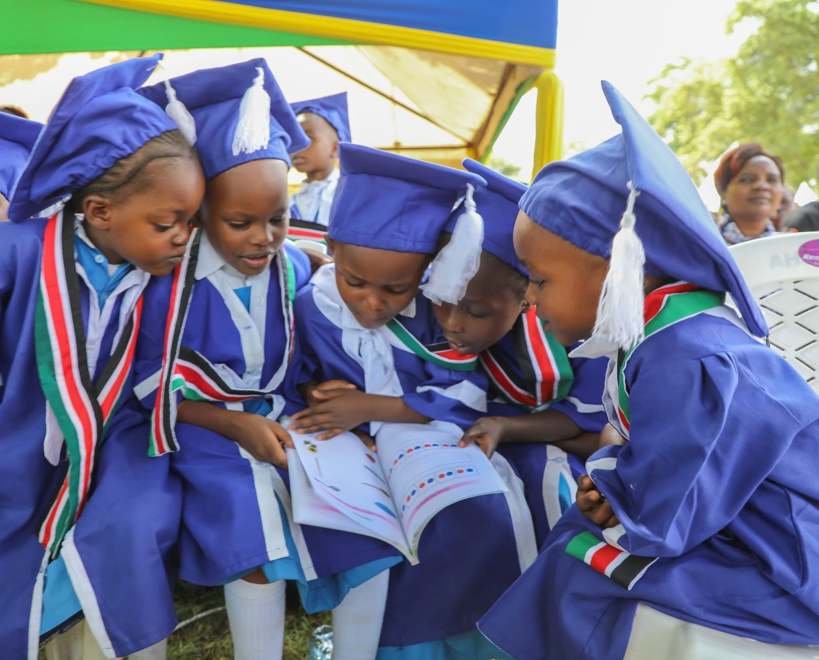 ECDE graduates in blue gowns reading a picture book together